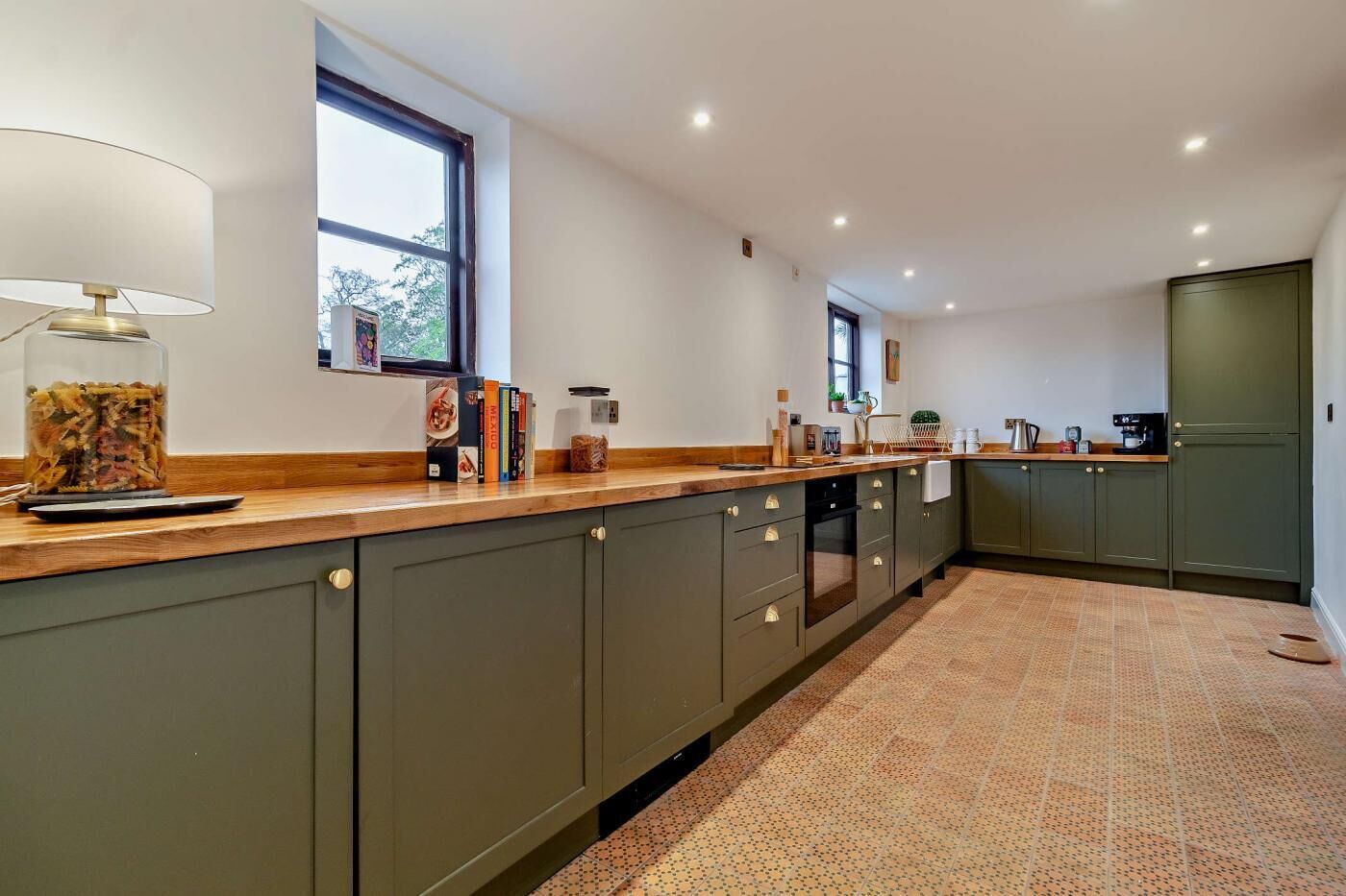 Une cuisine moderne avec des meubles de couleur vert foncé, un plan de travail en bois et un sol carrelé.