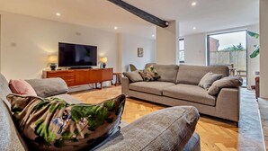 En moderne stue med et stort fladskærms-tv, et træskab og en sofa med blomstermønstrede puder.