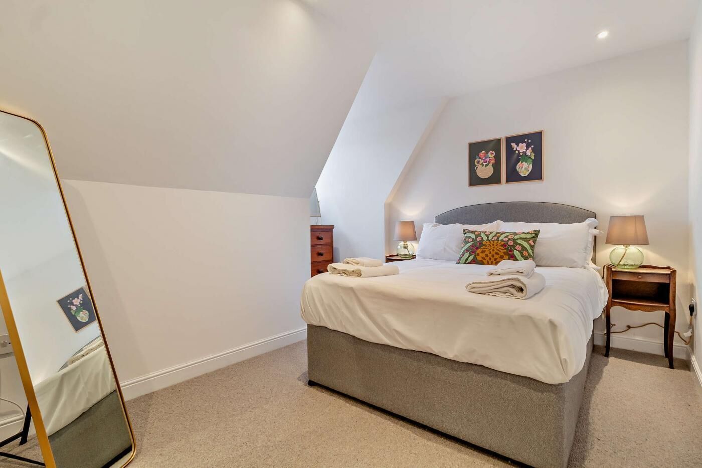 A neatly arranged bedroom with a bed, bedside tables, and a mirror.