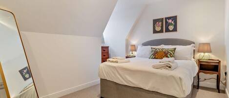 A neatly arranged bedroom with a bed, bedside tables, and a mirror.