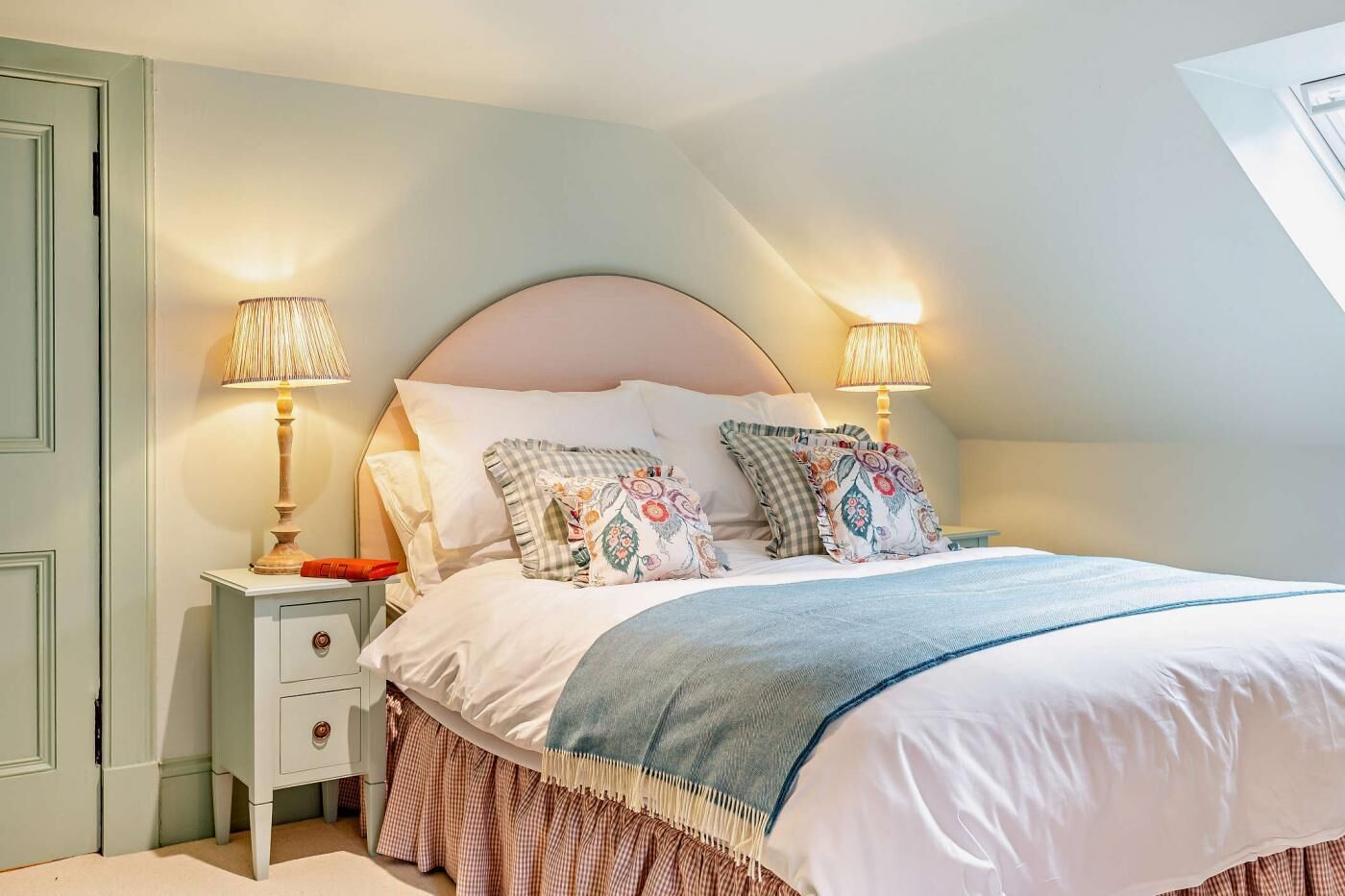 A bedroom with a bed, two bedside tables, a nightstand, a checkered skirt, and a lamp.