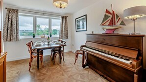 A dining area with a piano, a table set for four, and a window with curtains. - 2 Bed in Hudswell (oc-w28429) (Hudswell)