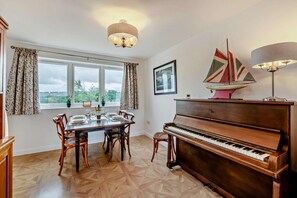 A dining area with a piano, a table set for four, and a window with curtains. - 2 Bed in Hudswell (oc-w28429) (Hudswell)