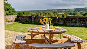 A round wooden picnic table with attached benches, a vase with sunflowers, and two glasses of orange juice. - 2 Bed in Hudswell (oc-w28429) (Hudswell)