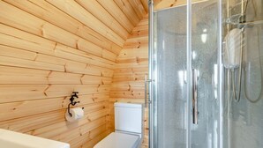 Ein Badezimmer mit Holzwandverkleidung, einer Toilette, einer Duschkabine aus Glas und einem Waschbecken.