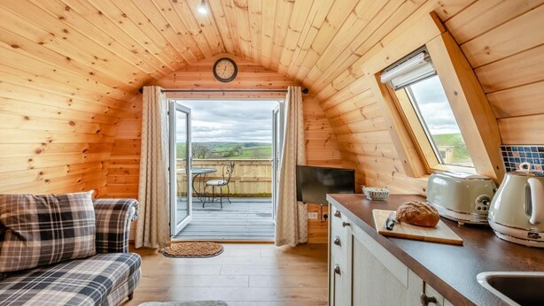 Ein gemütliches Blockhaus mit Holzvertäfelung, einem Essbereich mit Tisch und Stühlen, einer Küche mit Spüle und Geräten sowie einem großen Fenster mit Blick ins Freie.