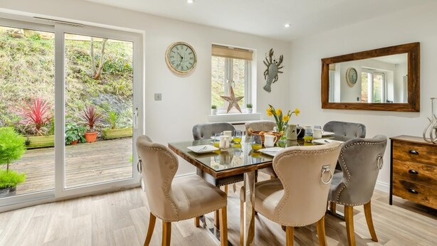 Un coin repas avec une table en verre, quatre chaises, une horloge et un miroir au mur.