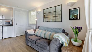 Een compacte woonruimte met een kitchenette, een bank, een spiegel en een lijst met een afbeelding aan de muur.