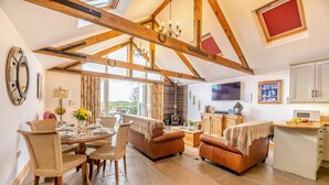 A spacious living area with a high ceiling, wooden beams, a fireplace, and a dining area with wicker furniture. - 2 Bed in Seahouses (oc-t19165) (Bamburgh)