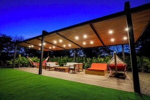 An outdoor patio area with a wooden deck, seating arrangements, and a covered section with lights. - Luxury Villa w Pool: Beach Club, FREE Golf & Maid (Pinilla)