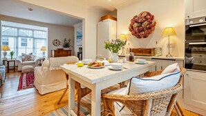A dining area with a white table, wicker chairs, and a kitchen in the background. - 3 Bed in Padstow (oc-b28803) (Padstow)
