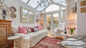 A conservatory with a white sofa, patterned cushions, a patterned rug, and a dining table with a vase of flowers. - 3 Bed in Padstow (oc-b28803) (Padstow)