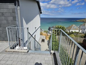 En trappa som leder upp till en balkong med utsikt över havet, en skylt med texten ”LOWER CHY-AN-MEOR” och ett metallräcke.
