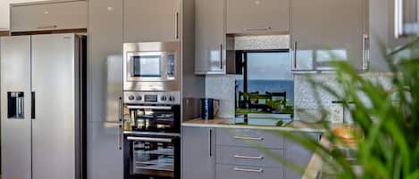 Une cuisine moderne dotée d’appareils électroménagers intégrés, de meubles de couleur grise et offrant une vue sur la mer.