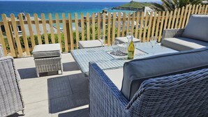 A patio with wicker furniture, a table with a bottle, and a view of the ocean. - 4 Bed in St. Ives (oc-c28788) (St Ives)