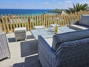 A patio with wicker furniture, a table with a bottle, and a view of the ocean. - 4 Bed in St. Ives (oc-c28788) (St Ives)
