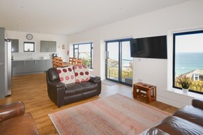 A modern living room with a leather sofa, a flat-screen TV, and a view of the sea. - 4 Bed in St. Ives (oc-c28788) (St Ives)