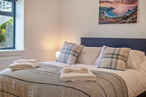 Ein ordentlich bezogenes Bett mit gestreifter Tagesdecke, zwei Kissen und gefalteten Handtüchern an der Kopfteil.