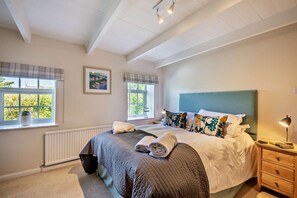 A bedroom with a large bed, two windows with curtains, a radiator, and a bedside table with a lamp. - 4 Bed in Craster (oc-t28831) (Dunstan)