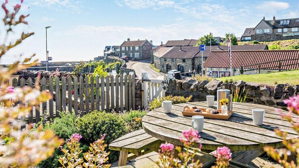 A coastal town with stone buildings, a wooden fence, and a picnic table with food and drinks. - 4 Bed in Craster (oc-t28831) (Dunstan)