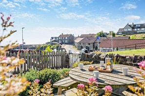 A coastal town with stone buildings, a wooden fence, and a picnic table with food and drinks. - 4 Bed in Craster (oc-t28831) (Dunstan)