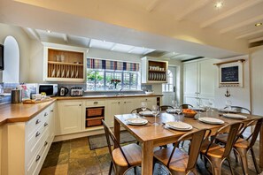 A spacious kitchen with a central island, wooden cabinets, and a dining area set for six. - 4 Bed in Craster (oc-t28831) (Dunstan)