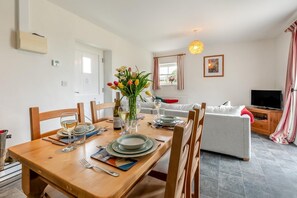 A dining area with a wooden table set for four, a vase of tulips, and a television in the background. - 2 Bed in Ponsanooth (oc-f28845) (Saint Gluvias)