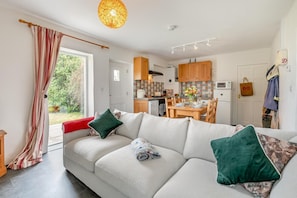 A modern living room with a sofa, a dining table, and a kitchen in the background. - 2 Bed in Ponsanooth (oc-f28845) (Saint Gluvias)