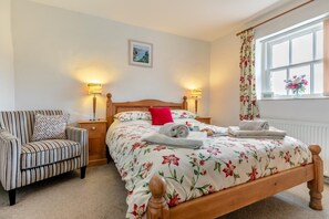 A bedroom with a bed, a chair, bedside tables, lamps, a window with curtains, and a picture on the wall. - 2 Bed in Ponsanooth (oc-f28845) (Saint Gluvias)