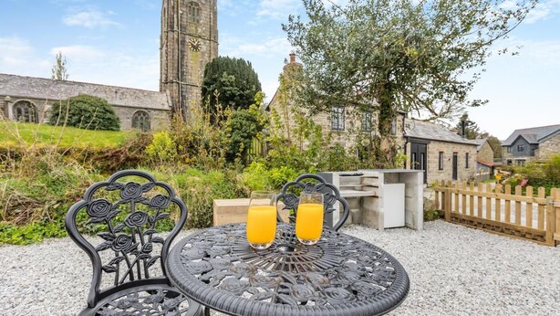 A table with two glasses of orange juice, a metal chair, and a stone building in the background. - 1 Bed in Cardinham (oc-s28796) (Cardinham)