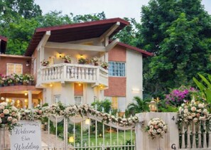 A two-story building with a balcony, surrounded by lush greenery and a decorative archway with a wedding welcome sign. - Holistic Wealth Retreat - On the Holistic Wealth Trail w/Pool -Belvedere Jamaica (Kingston)