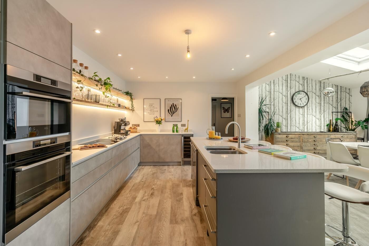 A modern kitchen with built-in appliances, a central island with a sink, and a dining area with a white table and chairs.
