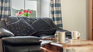 Un divano in pelle nera con cuscini decorati, un tavolino in legno e una tazza bianca.