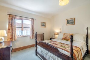 Un dormitorio con una cama de madera, una mesita de noche, una lámpara, un ventanal con cortinas y dos cuadros en la pared.