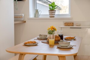 Une table de petit-déjeuner avec des croissants, un verre de jus d’orange et un vase rempli de fleurs jaunes.
