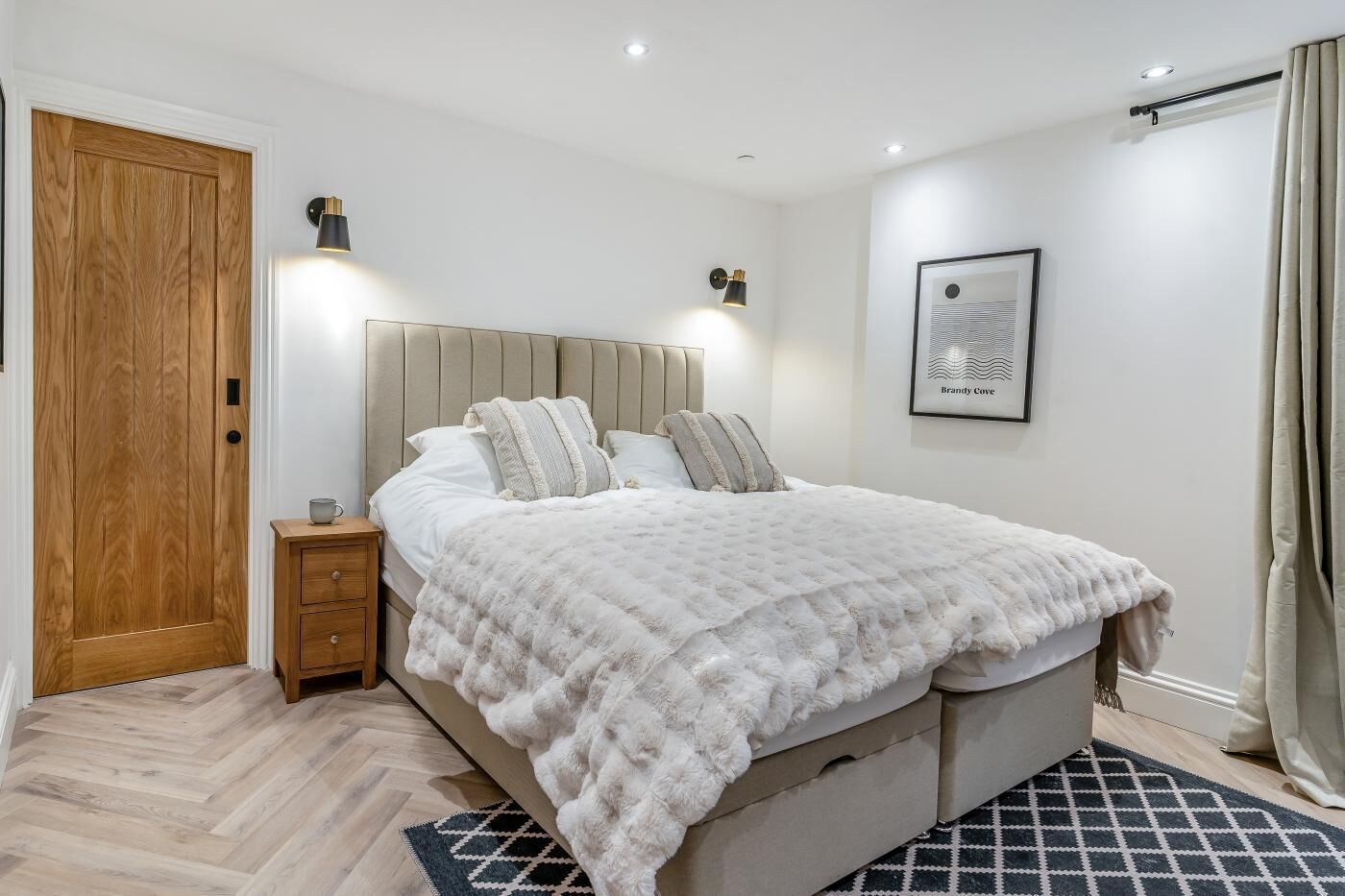 Une chambre à coucher avec un grand lit, une porte en bois, une table de chevet et un tableau encadré au mur.