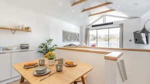 A modern kitchen with a wooden table set for breakfast, a large window, and a TV mounted on the wall. - 2 Bed in Mumbles (oc-c28839) (The Mumbles)