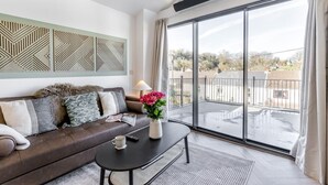 A modern living room with a brown leather sofa, a black coffee table, and a large window with a view of a residential area. - 2 Bed in Mumbles (oc-c28839) (The Mumbles)