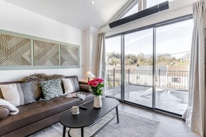 A modern living room with a brown leather sofa, a black coffee table, and a large window with a view of a residential area. - 2 Bed in Mumbles (oc-c28839) (The Mumbles)
