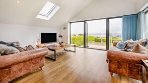 Ein geräumiges Wohnzimmer mit großem Fernseher, zwei Sofas, einem Couchtisch und Blick ins Freie durch große Glasüren.
