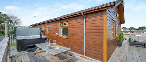 A wooden cabin with a hot tub, a table with glasses and a bottle, and a deck.
