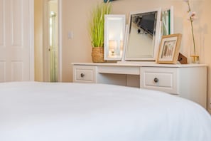 A bedroom with a bed, a dresser with drawers, a mirror, a framed picture, and a vase with a plant.