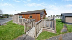 A small wooden cabin with a fenced deck, a paved pathway, and a grassy area. - 3 Bed in St. Merryn (oc-s28856) (Penrose)