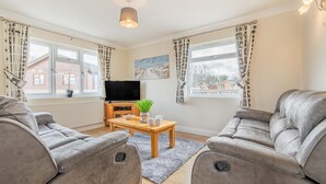 A living room with two grey sofas, a wooden coffee table, a TV, and a painting on the wall. - 3 Bed in St. Merryn (oc-s28856) (Penrose)