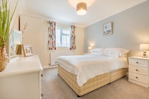 A bedroom with a bed, bedside tables, a radiator, curtains, a lamp, a framed picture, and a plant.