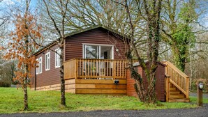 A wooden cabin with a deck, a staircase, and a grassy yard. - 1 Bed in Beaworthy (oc-h28859) (Highampton)