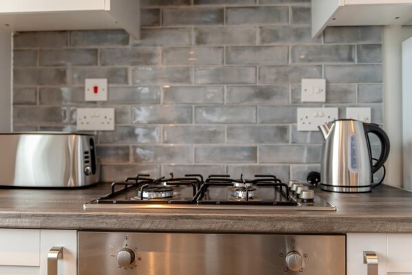 A kitchen with a gas stove, a toaster, and a kettle on a wooden countertop.