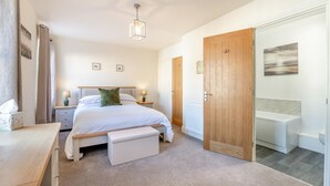 A bedroom with a bed, bedside tables, a bench, a wooden wardrobe, and a bathroom with a bathtub. - 4 Bed in Whitby (oc-b28403) (Whitby)