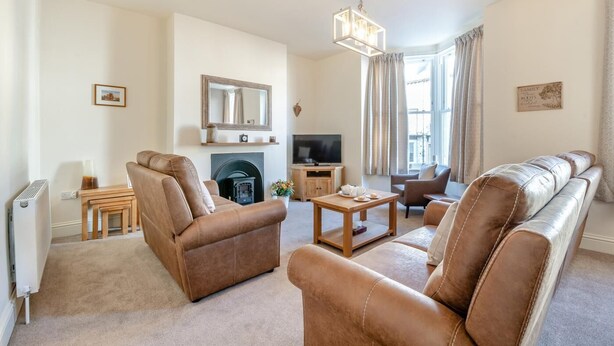 A living room with leather sofas, a fireplace, a television, and a chandelier. - 4 Bed in Whitby (oc-b28403) (Whitby)