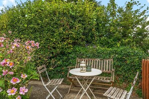Un giardino con una panchina di legno e un tavolo, circondato da vegetazione lussureggiante e piante in fiore.